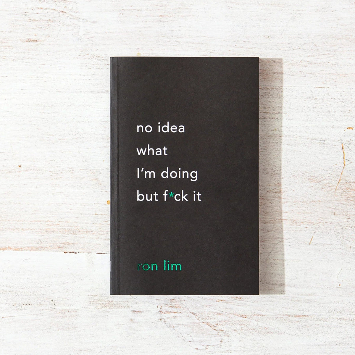 A black paperback book titled 'no idea what i'm doing but f*ck it' by Jon Lim, placed flat on a light, distressed wood background.
