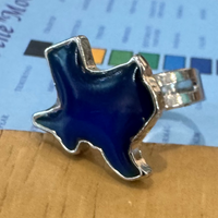A silver-toned ring with a blue enamel star-shaped face, resting on a light blue color card over a wooden tabletop.